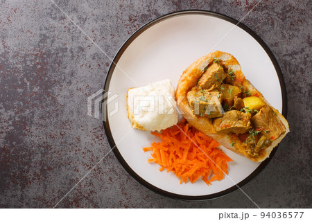 Closeup of lamb bunny chow the popular, Indian fast food cuisine which originated in South Africa, with carrot salad on plate. Horizontal top view 94036577