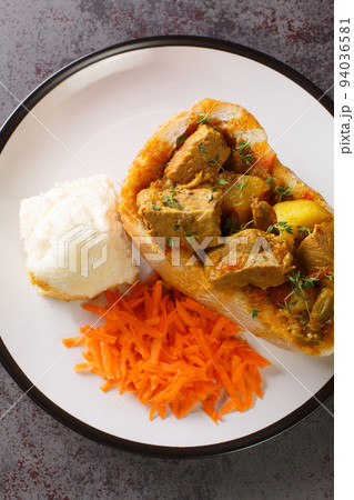 Durban Bunny Chow or a quarter mutton bunny consisting of a section of a loaf of bread hollowed out and filled with mutton curry and gravy closeup on plate. Vertical top view 94036581
