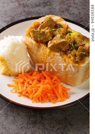 South African Bunny Chow bread stuffed with lamb curry with vegetables close-up on a plate. vertical 94036588
