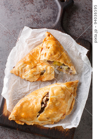 Traditional Cornish pasty filled with beef meat, potato and vegetables closeup on the paper. Vertical top view 94036595
