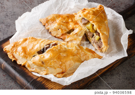Cornish Pasty Baked pie filled with meat and potatoes closeup on the wooden board. Horizontal 94036598