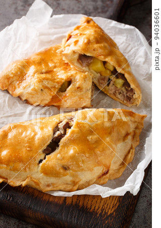 Traditional Cornish pasty filled with beef meat, potato and vegetables closeup on the paper. Vertical 94036601