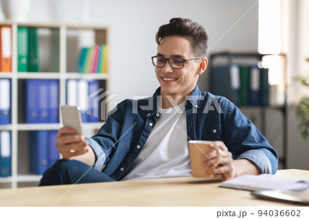 Young Male Office Employee Relaxing With Smartphone And Coffee At Workplace, 94036602