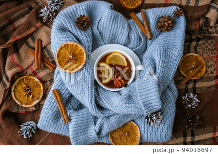 Blue sweater and cup of hot tea with lemon cinnamon sticks and anise star. Dry slices of citrus orange and cones. Hot winter cocktail. Christmas, Thanksgiving drinks. Autumn, grog, hot sangria, mulled 94036697