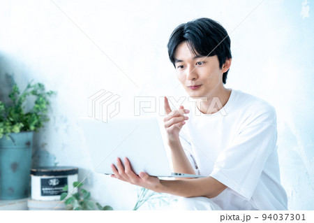 白壁の部屋でノートパソコンを使う若い男性 白壁の部屋でノートパソコンを使う若い男性 94037301