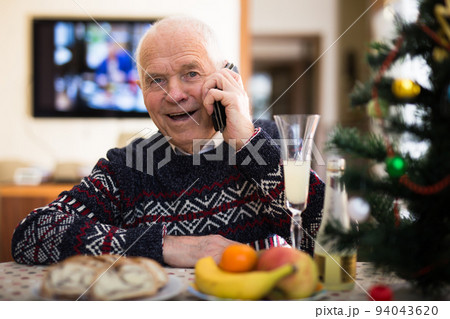 Happy elderly man talking on phone at table during Christmas celebration Happy elderly man talking on phone at table during Christmas celebration 94043620