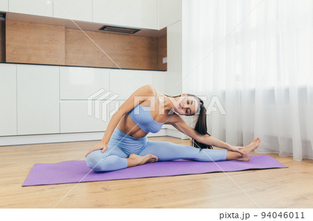 Sports time. Young beautiful fitness woman doing exercises at home on the mat, lifts her legs, shakes the press, squeezes 94046011