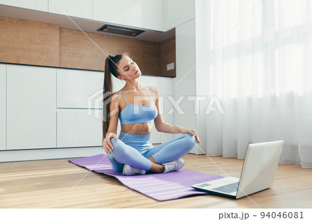 Time to train. Young beautiful woman fitness trainer doing workout online with laptop from home, sitting on mat, quarantine, isolation Time to train. Young beautiful woman fitness trainer doing workout online with laptop from home, sitting on mat, quarantine, isolation 94046081