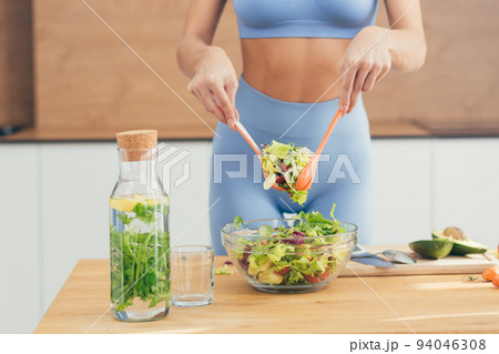 Close up photo, body part, hands of young fitness woman making salad with fresh vegetables and fresh detox drink in kitchen at home Close up photo, body part, hands of young fitness woman making salad with fresh vegetables and fresh detox drink in kitchen at home 94046308