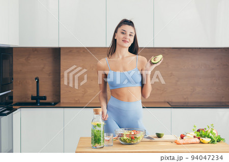 Young beautiful woman nutritionist teaches to cook online the Internet video call smartphone in the kitchen at home dish of fresh vegetable salad, looking at the camera, smiling Young beautiful woman nutritionist teaches to cook online the Internet video call smartphone in the kitchen at home dish of fresh vegetable salad, looking at the camera, smiling 94047234