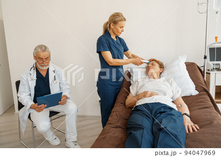 Close up of doctor measures patient's temperature with non-contact thermometer in hospital ward Close up of doctor measures patient's temperature with non-contact thermometer in hospital ward 94047969