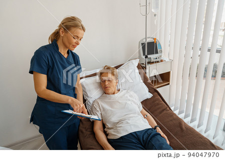 Nurse in uniform explain to patient results of analysis standing in hospital ward Nurse in uniform explain to patient results of analysis standing in hospital ward 94047970