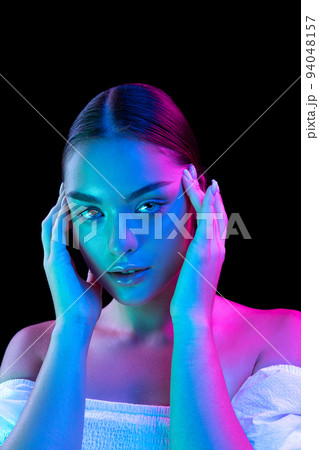 Closeup young beautiful woman with well-kept skin and sophisticated facial features isolated over dark background in purple neon light. 94048157