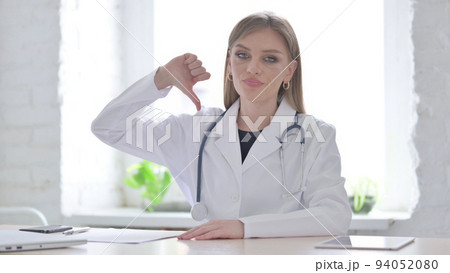 Lady Doctor Showing Thumbs Down While sitting in Clinic Lady Doctor Showing Thumbs Down While sitting in Clinic 94052080