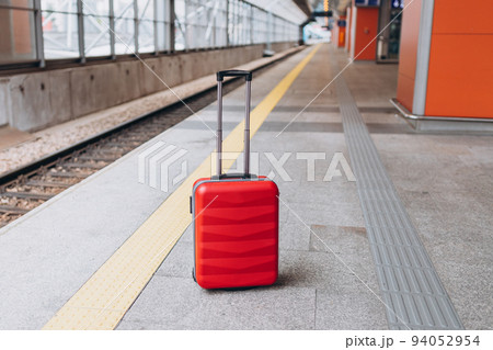 Forgotten travel bag on the train station. Red suitcase on empty station platform. Travel and vacation theme background. Travel banner 94052954