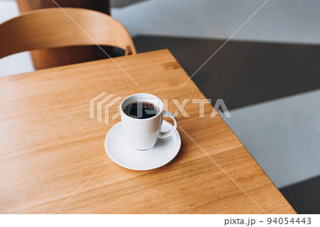 A Cup of freshly brewed black tea at a cafe blurred background. Coffee cup on table cafe shop Interior. Concept of easy breakfast. One white big ceramic cup. Top view. Alternative brewing methods A Cup of freshly brewed black tea at a cafe blurred background. Coffee cup on table cafe shop Interior. Concept of easy breakfast. One white big ceramic cup. Top view. Alternative brewing methods 94054443