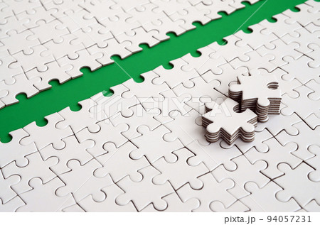 The green path is laid on the platform of a white folded jigsaw puzzle. The missing elements of the puzzle are stacked nearby. Texture image with space for text The green path is laid on the platform of a white folded jigsaw puzzle. The missing elements of the puzzle are stacked nearby. Texture image with space for text 94057231