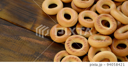 A lot of fresh yellow bagels lie on the surface of the old dark wood. A popular kind of flour products. One of the traditional Russian treats for tea 94058421