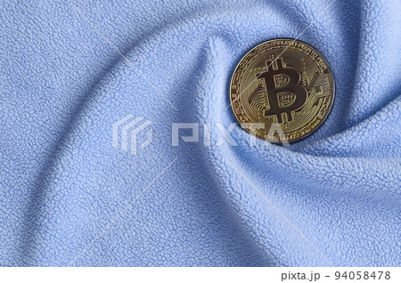 The golden bitcoin lies on a blanket made of soft and fluffy light blue fleece fabric with a large number of relief folds. The shape of the folds resembles a fan from a video card cooler 94058478