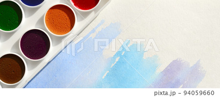 A new set of watercolors lies on a sheet of paper, which shows an abstract watercolor drawing in the form of blue strokes. The concept of amateur painting among teenagers A new set of watercolors lies on a sheet of paper, which shows an abstract watercolor drawing in the form of blue strokes. The concept of amateur painting among teenagers 94059660
