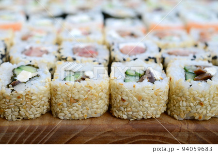Close-up of a lot of sushi rolls with different fillings lie on a wooden surface. Macro shot of cooked classic Japanese food with a copy space 94059683