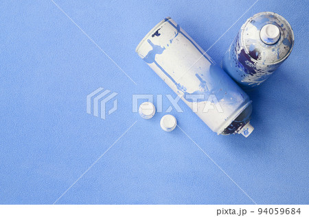 Some used blue aerosol spray cans and nozzles with paint drips lies on a blanket of soft and furry light blue fleece fabric. Classic female design color. Graffiti hooliganism concept 94059684