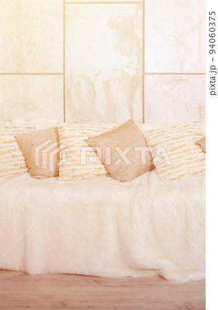 Many pillows lie on the couch, which is covered with a large plush veil against the background of a marble wall 94060375