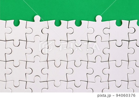 Fragment of a folded white jigsaw puzzle on the background of a green plastic surface. Texture photo with copy space for text 94060376