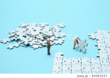 水色背景に白いパズルを組み立てる作業員と説教する会社員のフィギア 94063037
