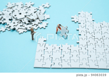水色背景に白いパズルを組み立てる作業員と説教する会社員のフィギア 94063039