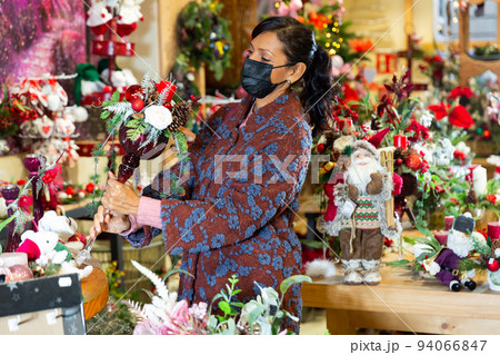 Latin woman in mask choosing christmas decorations Latin woman in mask choosing christmas decorations 94066847