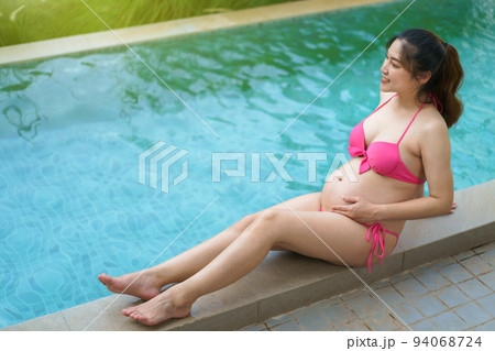 happy pregnant woman in bikini sitting on edge of swimming pool 94068724