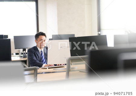 閑散としたオフィスでPC作業をするスーツ姿のビジネスマン 閑散としたオフィスでPC作業をするスーツ姿のビジネスマン 94071705
