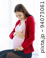 Pregnant woman sits on the bed in her bedroom, caressing her belly with a happy, smiling face. 94073061