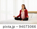 Pregnant woman sits in bed in her bedroom meditating alone in peace and happiness. The new mother resting by sitting down to chill out. 94073066