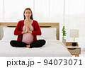 Pregnant woman sits in bed in her bedroom meditating alone in peace and happiness. The new mother resting by sitting down to chill out. 94073071