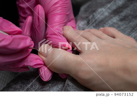 Podiatrist makes a pedicure to a client. The master conducts hygiene of the toes with a metal stick. 94073152