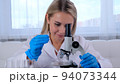 Female laboratory assistant analyzes samples using a microscope while working at a table in a 94073344