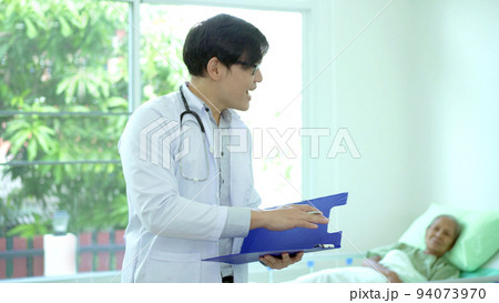 Asian doctor reading a medical document on notepad in hospital treatment ward. Health care and wellbeing concept. 94073970