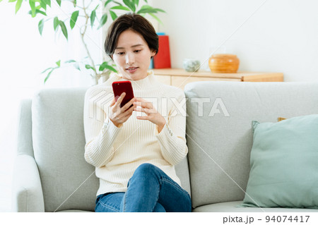 ソファでスマートフォンを見る女性 94074417