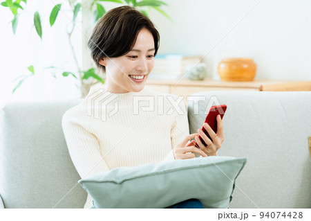 ソファでスマートフォンを見る女性 94074428