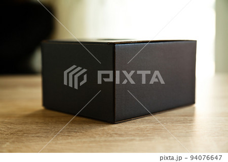 Closed rectangular cardboard box with corrugated cardboard lid, on oak wooden table 94076647