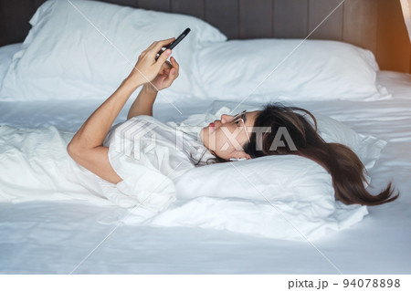 woman using smartphone for social media, young female watching movies by mobile phone on bed at home. technology, network, online shopping, e commerce, lifestyle and digital communication concept 94078898
