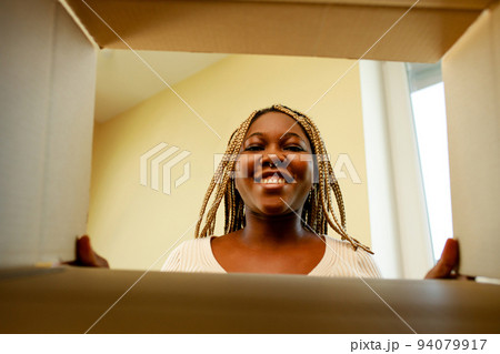 happy african american woman looking inside of box and surprised of cute pet 94079917