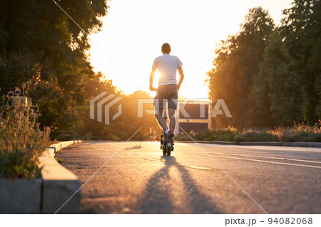 Man is riding on electric scooter or e-scooter on the street on the sunset. 94082068