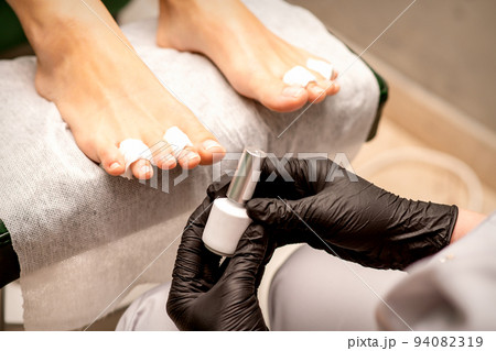 White nail polish in the hands of a manicurist while painting nails on a female feet, closeup 94082319
