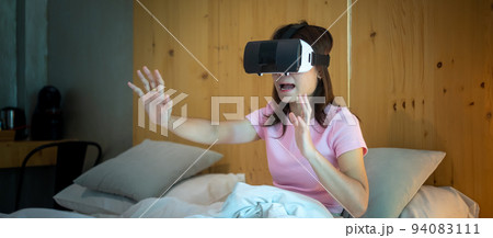 Young woman using virtual reality headset in bed. VR, Future digital technology, game, movies entertainment, metaverse, NFT and 3D cyberspace concept 94083111