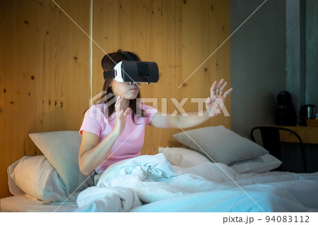 Young woman using virtual reality headset in bed. VR, Future digital technology, game, movies entertainment, metaverse, NFT and 3D cyberspace concept Young woman using virtual reality headset in bed. VR, Future digital technology, game, movies entertainment, metaverse, NFT and 3D cyberspace concept 94083112