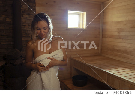 A young woman relaxes and sweats in a hot sauna wrapped in a towel. girl in the sauna. Finnish sauna interior, classic wooden sauna with hot steam. Russian bath. A young woman relaxes and sweats in a hot sauna wrapped in a towel. girl in the sauna. Finnish sauna interior, classic wooden sauna with hot steam. Russian bath. 94083869