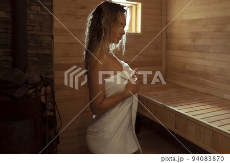 A young woman relaxes and sweats in a hot sauna wrapped in a towel. girl in the sauna. Finnish sauna interior, classic wooden sauna with hot steam. Russian bath. A young woman relaxes and sweats in a hot sauna wrapped in a towel. girl in the sauna. Finnish sauna interior, classic wooden sauna with hot steam. Russian bath. 94083870
